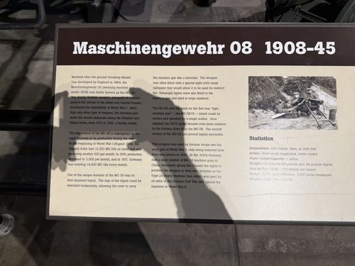 An angled close-up of the placard for the German Maschinengewehr 08 machine gun, with a black-and-white photo of the gun on its sledge mount and a Statistics box. The sign is shot at a sharp diagonal but the title and most body text are legible.