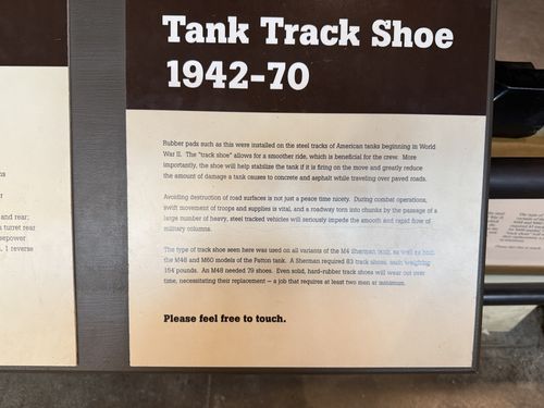 Placard titled 'Tank Track Shoe 1942-70' explaining the rubber-padded steel track shoe, with a 'Please feel free to touch.' invitation at the bottom.