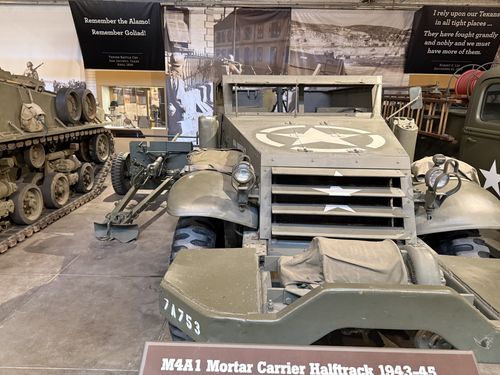 The M4A1 mortar carrier halftrack itself, front view, hull number 7A753, with a big white star on the slatted radiator. Behind it sit a US light tank and a towed anti-tank gun, under 'Remember the Alamo! Remember Goliad!' and Robert E. Lee quote banners.