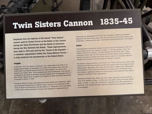 Close-up of the large 'Twin Sisters Cannon 1835-45' placard, a brown-and-cream two-column panel mounted on a metal stand above the cannon. Full body text legible.