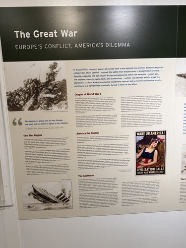 Wall panel titled 'The Great War - Europe's Conflict, America's Dilemma', with a 'WAKE UP AMERICA!' poster of a sleeping woman, a sinking ship illustration, and sections headed 'Origins of World War I', 'The War Begins', 'America the Neutral', and 'The Lusitania'.
