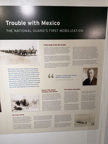 Wall panel titled 'Trouble with Mexico - The National Guard's First Mobilization', with photos of mounted cavalry and Pancho Villa, a portrait of President Woodrow Wilson, and sections headed 'Crisis South of the Rio Grande', 'Pancho Villa attacks Columbus, New Mexico', 'The Punitive Expedition', and 'The Great Call Up'.
