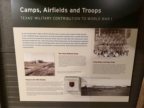 Wall panel titled 'Camps, Airfields and Troops - Texas' Military Contribution to World War I', with a photo of an automobile-mechanics school band, a small flag/insignia display case, and sections headed 'The Texas National Guard', 'Camp Mabry and Penn Field', and 'Texans in the 90th Division'.