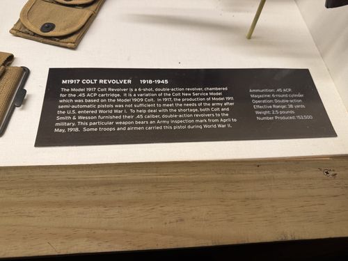 Close-up of the placard inside the weapons case for the M1917 Colt Revolver, with the revolver's holster and a magazine pouch partly visible above.