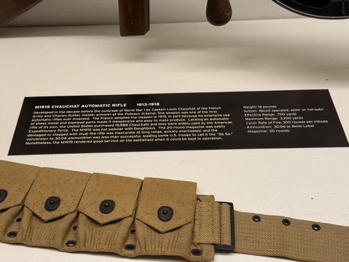 Close-up of the placard for the M1915 Chauchat Automatic Rifle, with the wooden stock of the gun above and a US cartridge belt below the sign.