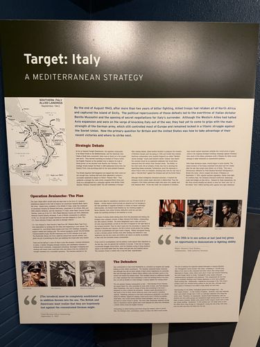 Large wall panel titled 'Target: Italy / A Mediterranean Strategy', with a map of the Southern Italy Allied Landings (September 1943), portrait photos of commanders, and columns under 'Strategic Debate', 'Operation Avalanche: The Plan', and 'The Defenders'.