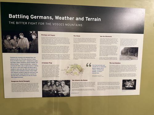 Wide wall panel titled 'Battling Germans, Weather and Terrain' with photos of soldiers in the field, a map of the Vosges/Alsace region, and several text columns including a section on the Lost Battalion and the 442nd.
