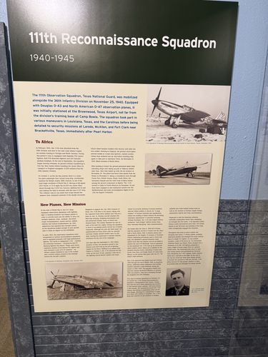 Tall printed wall panel titled '111th Reconnaissance Squadron 1940-1945' with sub-sections 'To Africa' and 'New Planes, New Mission'. Several black-and-white aircraft photos (including a fighter and light observation planes) and a portrait of an airman are on the right.