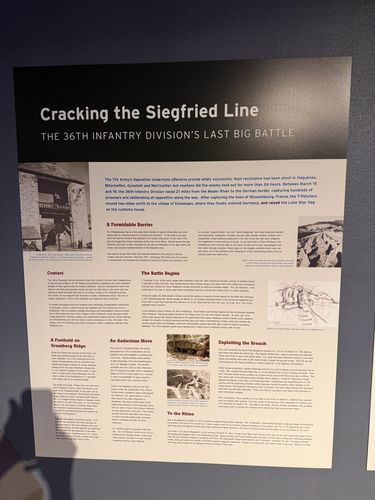 Straight-on photo of an interpretive panel titled 'Cracking the Siegfried Line - The 36th Infantry Division's Last Big Battle', with photos of fortifications and a battle map, and sections A Formidable Barrier, Contact, The Battle Begins, A Foothold on Grassberg Ridge, An Audacious Move, Exploiting the Breach, To the Rhine.