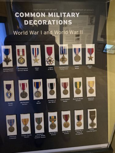Glass case titled 'Common Military Decorations - World War I and World War II' displaying 21 medals in three rows, each with a printed label naming the award.