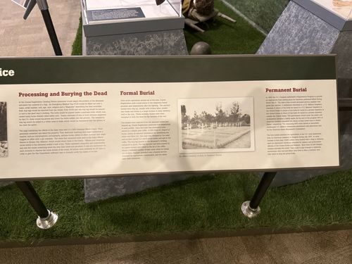 The right-hand portion of the same low Graves Registration Service placard, showing sections 'Processing and Burying the Dead', 'Formal Burial', and 'Permanent Burial', with a photo of an Allied cemetery.