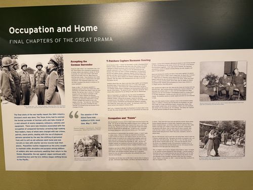 A long wall panel titled 'Occupation and Home - Final Chapters of the Great Drama', with several archival photographs (including soldiers and a captured German general), and sections Accepting the German Surrender, T-Patchers Capture Hermann Goering, and Occupation and 'Points', plus an Eisenhower pull-quote.