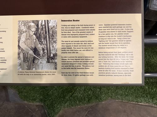 Right half of the same M135/mess-truck placard panel, titled 'Immersion Heater', explaining field sanitation, with a black-and-white photo captioned 'A veteran Texas National Guardsman cleans his mess kit with the help of an immersion heater, circa 1960.'