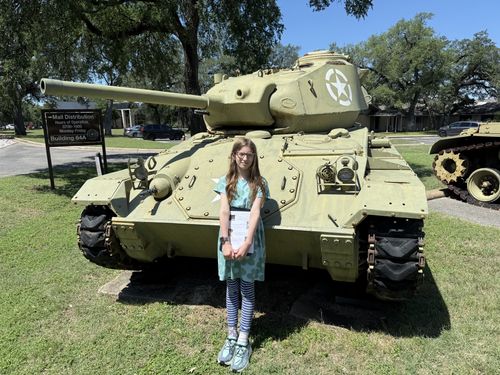 Maxine centered in front of the green light tank, packet in hand, the white star and bolt-studded hull plates clearly visible behind her. Sharp, well-lit frame.